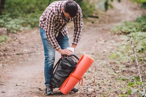 Hiker holding his camping backpack. traveler opening backpack while traveling in beautiful wood. Theme hiking and travel. Man traveling in forest with backpack. Active healthy man hiking in forest