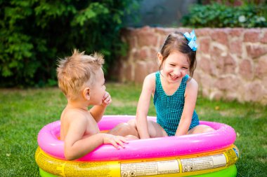 Two little brother and sister playing and splashing in pool on hot summer day. Children swimming in kid pool. Two cheerful cute children playing and having fun, splash in inflatable pool at backyard clipart