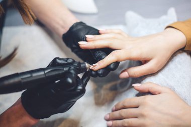 Profesyonel güzellik uzmanlarının elleri müşteri tırnaklarında elektrikli matkap ile çalışıyor. Yapay tırnakların uygulanması prosedürü. El manikürcüsü. Manikürcü eldivenleri tırnak etlerini çıkarıyor.