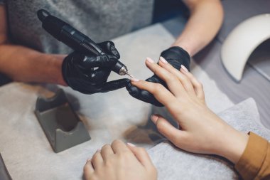 Güzellik Salonu, Manikür, Çivi Cila Prosedürü. Güzellik salonunda elektrikli makine kullanan profesyonel donanım manikürü. Usta manikür sırasında ojeli elleri kesmek için elektrikli makine kullanıyor.