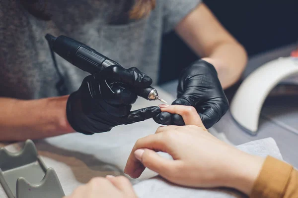 Close-up professional beautician hands working with electric drill file on client fingernails. Procedure applying artificial fingernails. Hands manicurist with tool. Manicurist gloves removes cuticle — Stock Photo, Image