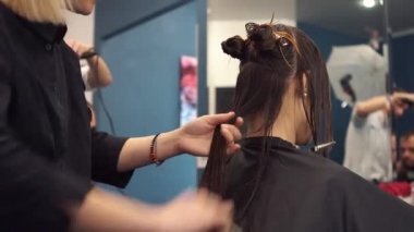 Kuaför elinde makas ve tarak tutuyor ve saçını kestiren kadın müşteri yapıyor. Güzellik salonunda genç ve güzel bir kadın saçı. Saç kesme işlemi makasla yapılır. Kuaför kahverengiyi buduyor.
