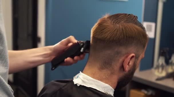 Tiro de perto de um homem a cortar o cabelo na barbearia. Cabeleireiro masculino servindo cliente, fazendo corte de cabelo usando máquina e pente — Vídeo de Stock