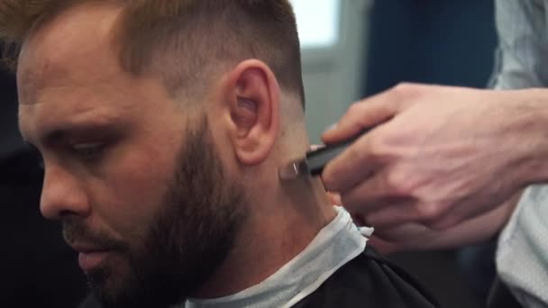 Nahaufnahme eines Mannes, der sich beim Friseur eine modische Frisur schneidet. männlicher Friseur bedient Klient, macht Haarschnitt mit Maschine und Kamm — Stockvideo