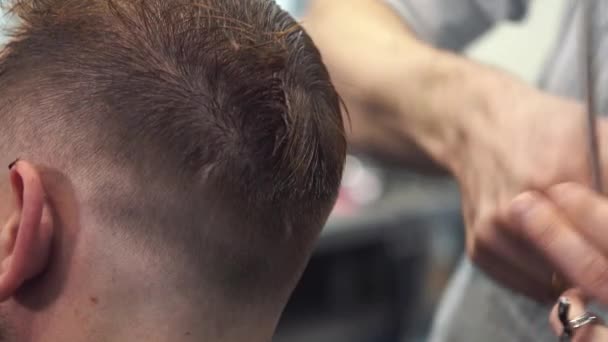Primer plano de hombre consiguiendo corte de pelo de moda en la peluquería. Peluquero masculino sirviendo cliente, haciendo corte de pelo usando máquina y peine — Vídeo de stock
