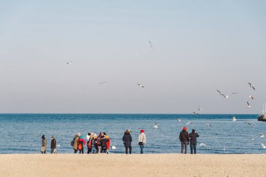 İnsanlar kışın kumsalda yürür. Mükemmel bir kış tatili. İnsanlar soğuk mevsimlerde kıyıda rahatlar. Gdansk, Polonya 9 Şubat 2020. Baltık Denizi kıyısındaki Sopot şehrinde yürüyen kalabalık..