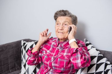 Tema eski kişi teknolojisini kullanır. Arama ve telefonda konuşurken evde oturma odasında kanepede oturan ve bir cep telefonu kullanarak olgun mutlu sevinç gülümseme etkin gri saç beyaz kırışıklıkları bir kadın