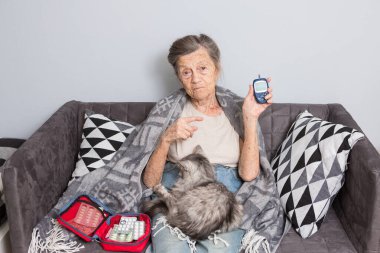 Mutlu yaşlı kadın evde glukometre kullanıyor. Yaşlı kadın diyabetik muayene, kollarında evcil hayvanla kan şekeri seviyesi. Glukometreyle Diyabet kavramı.