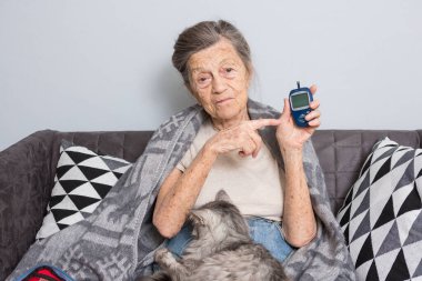 Mutlu yaşlı kadın evde glukometre kullanıyor. Yaşlı kadın diyabetik muayene, kollarında evcil hayvanla kan şekeri seviyesi. Glukometreyle Diyabet kavramı.