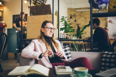 Kafede oturan güzel bir bayanın hayalindeki fikirler, yaratıcı bir meslek. temalı modern kadın blog yazarı. Elinde kalem olan genç bir kadın planlar üzerinde düşünüyor, birlikte çalışma alanında boş zaman yaratıyor..