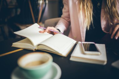 İş kadını Not Defteri Yazıyor. Defterine işaret koyan kadın ellerine yakın çekim. Şehir kahvehanesinde işyeri. Kadın işadamı öğle yemeğinde çalışıyor. Bağımsız blog yazarı gazeteci iş başında