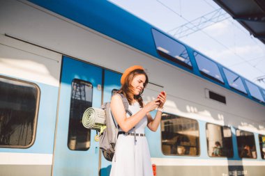 İstasyonda akıllı telefon kullanan gülümseyen kadın. Akıllı telefon tutan ve tren istasyonunda duran genç bir kadın. Tema Taşımacılık ve Seyahat. yolculuk konsepti.