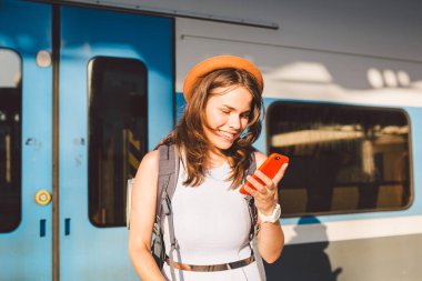 İstasyonda akıllı telefon kullanan gülümseyen kadın. Akıllı telefon tutan ve tren istasyonunda duran genç bir kadın. Tema Taşımacılık ve Seyahat. yolculuk konsepti.