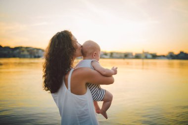Aile ve bekar anne kavramı, oğul ve öpücük taşıyan kadınlar. Mutlu aile kavramı. Yakın çekim. Bir annenin portresi. Oğlu kucaklıyor ve öpüyor. Yazın nehir kenarında, doğada..