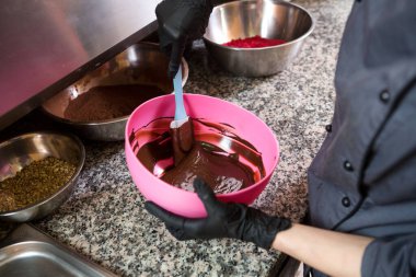 Çikolata pişirme teması. Bir ele yakın çekim. Genç beyaz kadın dövmeli ve üniformalı aşçı sıcak kalın çikolatayı tencerede yapmaya hazırlanıyor. Pasta şefi mutfakta sıvı çikolata karıştırıyor..