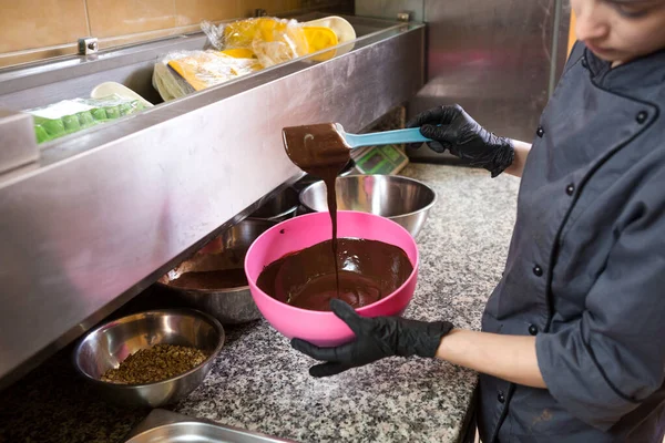 Theme cooking chocolate. Close-up of a hand. Young Caucasian woman cook with tattoo and in uniform prepares to make hot thick chocolate in a pot. Pastry chef mixes liquid chocolate in the kitchen.