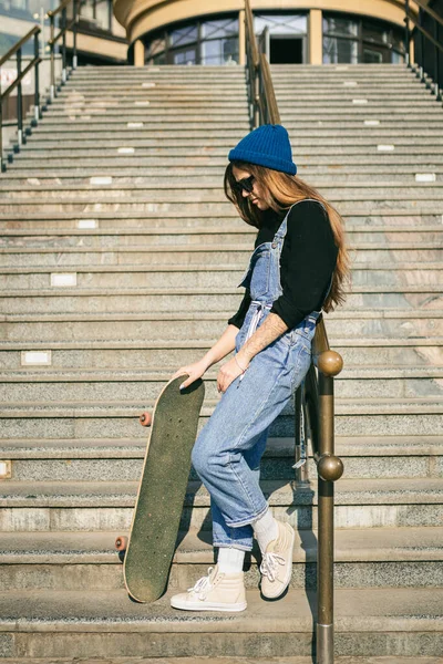 スケートボードを手に路上でポーズを若い白人女性 都会の中で青いジーンズの極端なスポーツで10代の女の子 若者のレクリエーション ライフスタイルのテーマ 市内のスケートボーダー — ストック写真