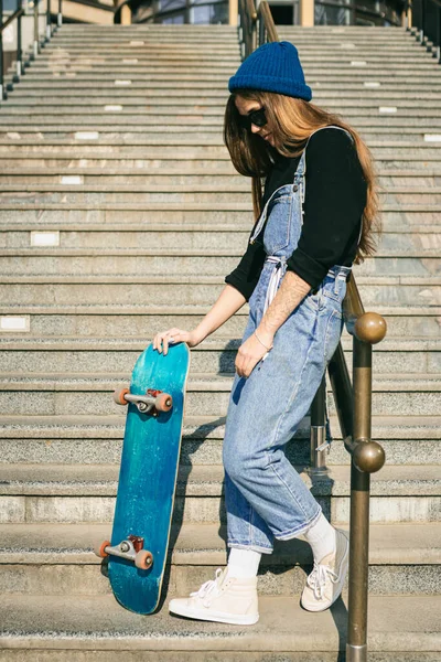 スケートのある都会の女性 街でスケートボードとヒップスターの女の子 極端なスポーツと感情の概念 代替ライフスタイル スケートボードとポージングを保持スタイリッシュなヒップスターの女の子 ストリートスタイルの衣装 — ストック写真