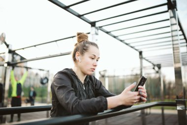 Güzel atletik kadın sabahları dışarıda, yorgun sporcu kadın kablosuz kulaklıkla müzik dinliyor. Sporcu fit kız antrenmandan sonra dinleniyor. Spor tarzı Bluetooth kulaklıklar.