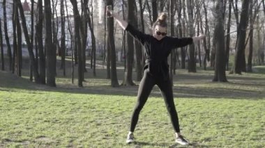 Parkta spor yaparken cep telefonu kullanan çekici bir kadın. Sağlıklı genç bir kadın dışarıda ısınıyor. Akıllı telefondaki sosyal ağlardaki yazışmalar dikkatini dağıtıyor. sağlıklı fitness yaşam tarzı