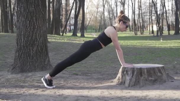 Fitte Frau, die im Wald Liegestütze auf einem Baumstamm macht. Bewegung im Freien in der natürlichen Turnhalle. Liegestütze. Attraktive Sportlerin, die im Park Liegestütze macht. Training im Freien — Stockvideo