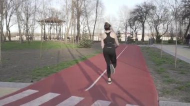 Genç bayan koşucu parkta koşu pistinde koşuyor. Aktivite, insan. Koşucu koşu pistinde koşuyor. Vücudu çok iyi durumda tutuyor. Yürümek ve koşmak için lastik bantlı pist