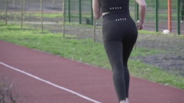 Genç beyaz bir kadın, kırmızı lastik bir yolda parkta koşuyor. Kız sporcu şehirde kardiyo çalışması yapıyor. Hareket hayattır. Şehir parkında koşan sporcu kadın.