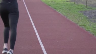 Genç bayan koşucu parkta koşu pistinde koşuyor. Aktivite, insan. Koşucu koşu pistinde koşuyor. Vücudu çok iyi durumda tutuyor. Yürümek ve koşmak için lastik bantlı pist