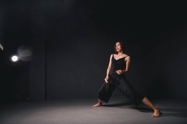 Siyah arka planda dans eden güzel bir kadının portresi. Karanlık zeminde dans eden bale ve çağdaş dansçı. Çağdaş Sanat. Siyah elbiseli, siyah duvarda poz veren plastik ve esnek bir kız..