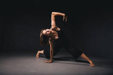Siyah arka planda dans eden güzel bir kadının portresi. Karanlık zeminde dans eden bale ve çağdaş dansçı. Çağdaş Sanat. Siyah elbiseli, siyah duvarda poz veren plastik ve esnek bir kız..