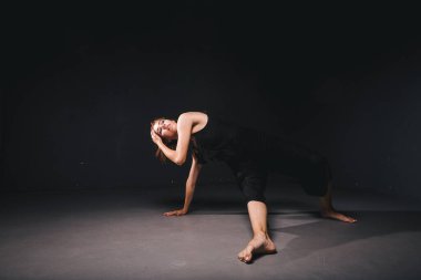 Siyah arka planda dans eden güzel bir kadının portresi. Karanlık zeminde dans eden bale ve çağdaş dansçı. Çağdaş Sanat. Siyah elbiseli, siyah duvarda poz veren plastik ve esnek bir kız..