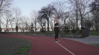 Tema akrobatik egzersiz. Genç, beyaz bir kadın parkta lastik bir pistte takla atıyor. Kız takla atıyor. Sporcu, spor egzersizi yapıyor. Açık hava jimnastiği