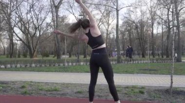 Tema akrobatik egzersiz. Genç, beyaz bir kadın parkta lastik bir pistte takla atıyor. Kız takla atıyor. Sporcu, spor egzersizi yapıyor. Açık hava jimnastiği