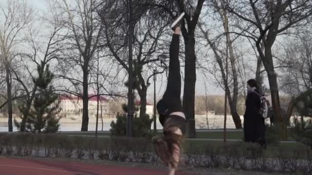 Le thème est l'exercice acrobatique. Jeune femme du caucasien faisant un tour La roue dans le parc sur une piste de course en caoutchouc. fille faisant de la cartwheel. Femme sportive faisant des exercices physiques. gymnastique en plein air — Video