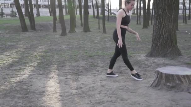 Uma jovem caucasiana faz um suporte em uma área arborizada, apoiando as mãos em um toco. Estilo de vida saudável feminino Prática Handstand On Park. Desportista fazendo acrobacias de fitness — Vídeo de Stock