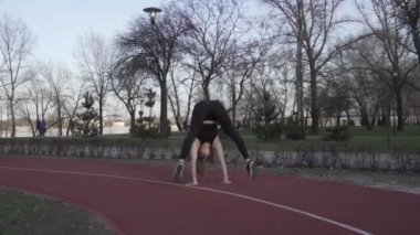 Şehir parkında jimnastik ve akrobasi. Uzun saçlı, dövmeli ve siyah spor kıyafetli genç bir kadın lastik koşu bandında egzersiz yapıyor. Spor kadın jimnastikçi elleri üzerinde yürüyor