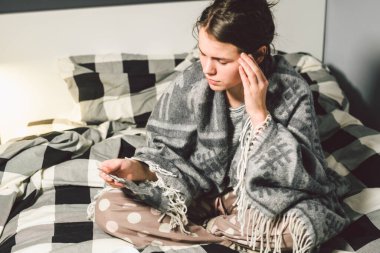 Denek hastalık ve tedavi. Kafkasyalı genç bir kadın yatak odasında yüksek ateşi olan bir battaniyeye sarılmış, ateşi baş ağrısına neden oluyor, sinüzit için burun içine ilaç koyuyor..