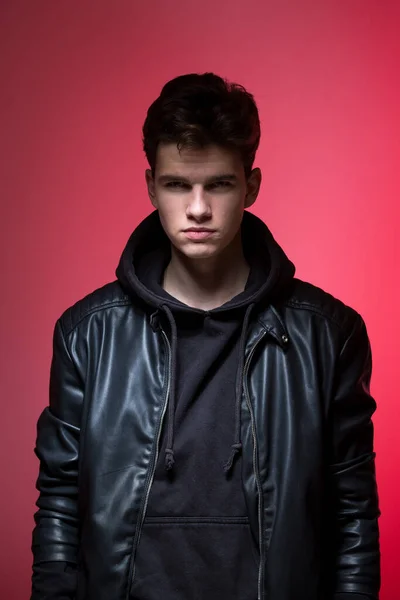Cute brutal man in black leather jacket model style. Portrait of a handsome guy on pink studio background. Man In Black Jacket. Young Fashion Man In Leather Jacket on a pink background.