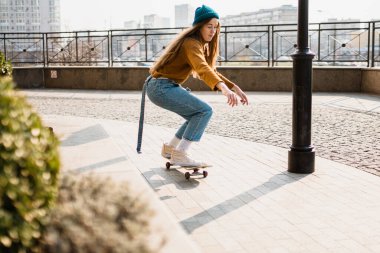 Kaykay süren genç ve güzel bir kadın. Şehir tarzında bir spor kadın modeli portresi. Şehirde kaykay yapmak. Sokak tarzı kıyafet. Şehir kadını paten kayıyor. Kaykaylı hippi kız.