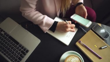 Kafeteryanın içindeki ahşap masaya beyaz kadın elini koy ve not defterine not al. Denek serbest yazar blogcu gazeteci iş başında. Tanımlanamayan kişi. Teknoloji telefonu ve fincan kahveli dizüstü bilgisayar.