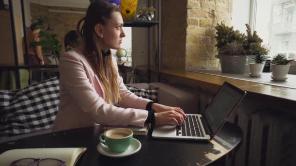 若くて美しい白人女性がコーヒーを飲んで、木製のテーブルでカフェの中でキーボードをタイピング。現代の職業の話題はブロガー、フリーランサー、ライター — ストック動画