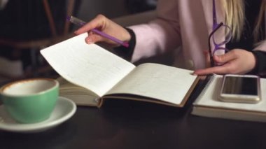 Bir kafede günlüğün sayfalarını karıştıran serbest çalışan bir kadın. Kafede çalışan bir girişimci. İş kadını kâğıt hatırlatıcıları ve programlar kullanır. Kız günlük tutuyor, iş planı yapıyor.