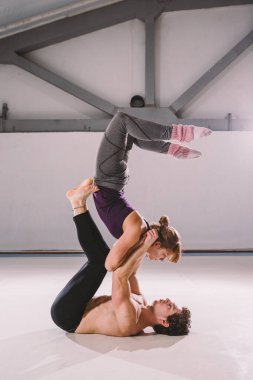 Akroyoga ve Yoga Pozisyonları teması. Akroyogiler pratik yapıyor. Stüdyo ışıklarıyla. Merkez 'in Statik' te tuttuğu adam, kadın Flyer 'ı kollarının arasında üstte konumlandırıyor. Pozisyon akrebi.