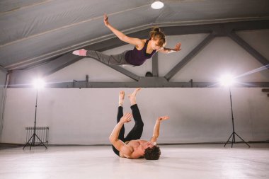 Genç çift spor salonunda akro yoga yapıyor. Sağlıklı bir yaşam tarzı. Akroyoga. Çift yogası. Ortak yogası. Kadınları havaya atan kaslı bir adam. Güven, güç ve cesaret kavramı.