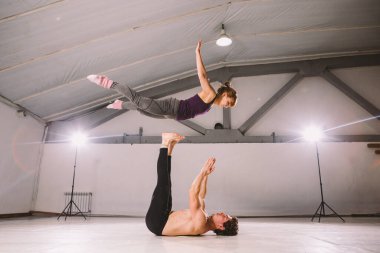 Genç çift spor salonunda akro yoga yapıyor. Sağlıklı bir yaşam tarzı. Akroyoga. Çift yogası. Ortak yogası. Kadınları havaya atan kaslı bir adam. Güven, güç ve cesaret kavramı.