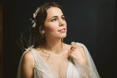 Düğün makyajı ve mücevher tacıyla güzel bir gelin. Evde gelin pozu. Güzel gelinin sabahı. Düğün günü. Yeni evli kadın düğün için son hazırlık. Kadın damadı bekler..