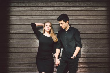 Siyah elbiseli, ahşap bir duvarın arkasında poz veren çok kültürlü bir çift. Türk adam ve Kafkas kadın flört ve aşk. Yaşam tarzı, bir çift aşık. Genç ve Özgür.