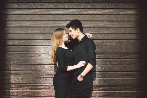 Multiracial stylish couple in black clothes posing on a background of a wooden wall. Turkish guy and caucasian girl date and love. Muslim man and gurney woman together.