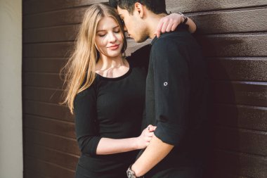 Siyah elbiseli, ahşap bir duvarın arkasında poz veren çok kültürlü bir çift. Türk adam ve Kafkas kadın flört ve aşk. Yaşam tarzı, bir çift aşık. Genç ve Özgür.