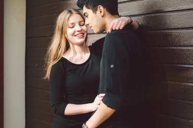 Siyah elbiseli, ahşap bir duvarın arkasında poz veren çok kültürlü bir çift. Türk erkek ve Kafkas kız buluşmaları ve aşkları. Müslüman adam ve sedye kadın birlikte..